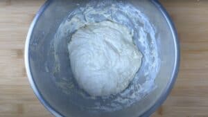 Bread dough rising in a metal bowl on a wooden surface, ready for baking.